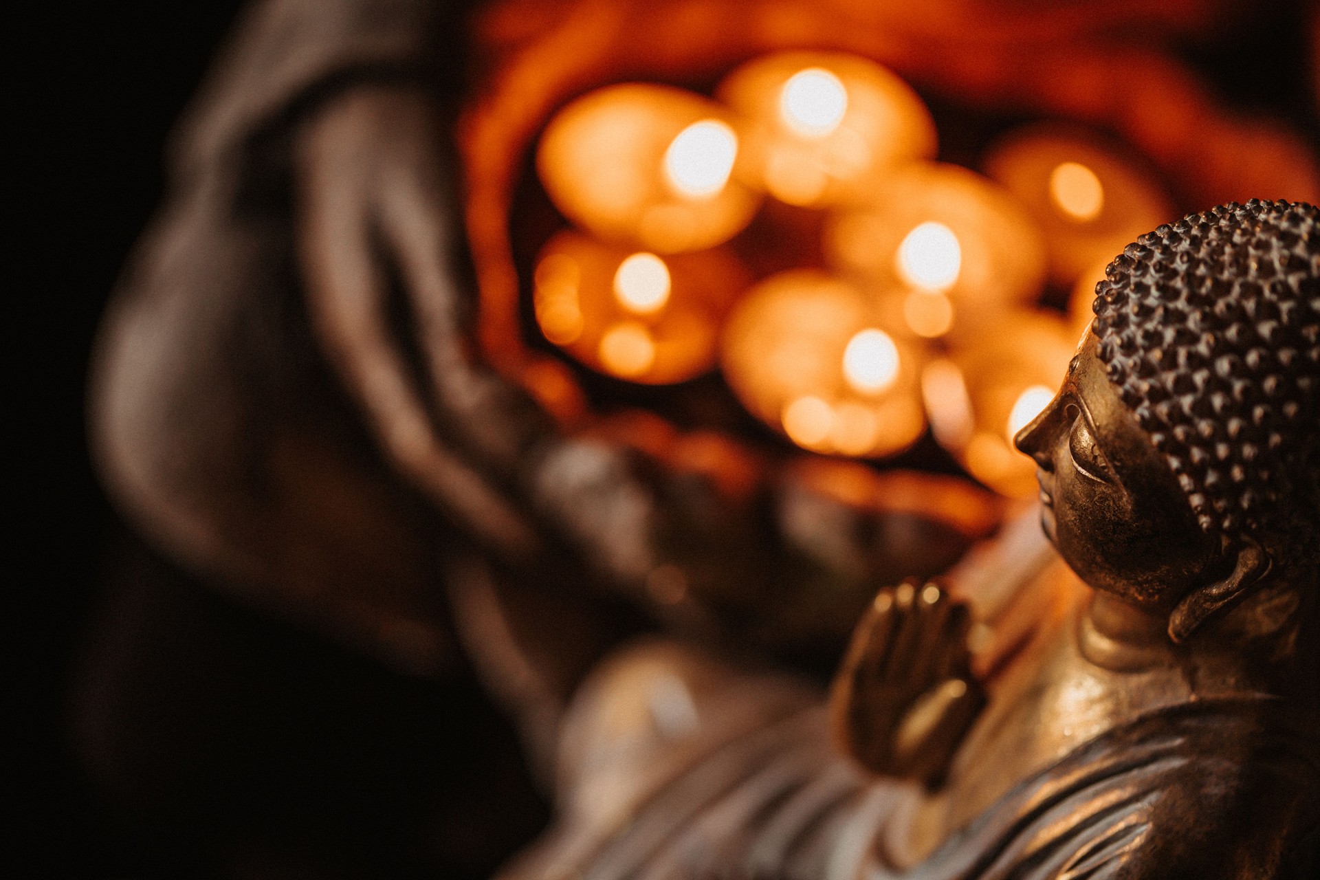 Close up of a buddha figurine seen slightly from the side and from above in front of lit candles