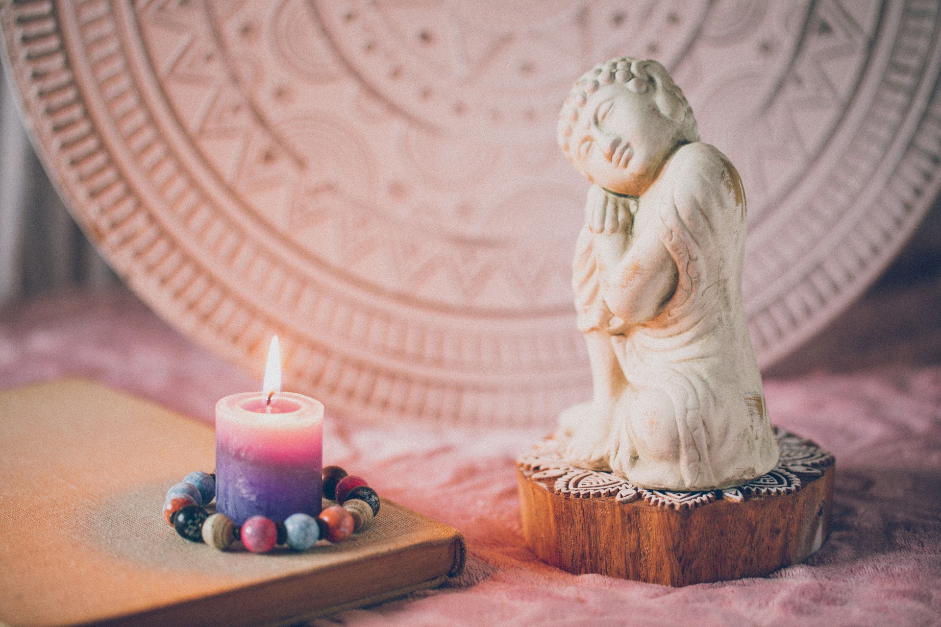 Buddha of compassion figurine with a book and a lighted candle in front of a white mandala in soft rose ambience